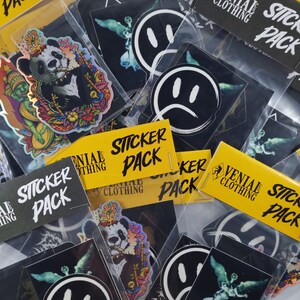 May include: A collection of sticker packs featuring various designs, including a panda, a smiley face, a sad face, and an angel. The sticker packs are labelled "Sticker Pack" and "Venial Clothing".