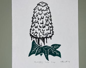 May include: Black and white line art print of a shaggy ink cap mushroom with green leaves. The print is titled "Shaggy Ink Cap" and signed "Catherine 22".