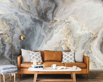 Peut inclure: Un canapé en cuir marron avec trois coussins, une table basse blanche avec des livres et une tasse, et un repose-pieds à motifs bleu et blanc. Le canapé est devant un mur avec un motif de marbre gris et or.
