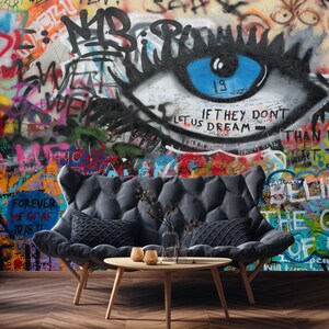 Pode incluir: Um sof&aacute; cinza com duas almofadas fica em frente a uma parede coberta de grafites coloridos. Os grafites apresentam um olho grande com uma &iacute;ris azul e o texto "IF THEY DON'T LET US DREAM THAN".
