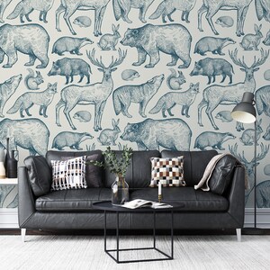 Puede incluir: Un papel tapiz azul y blanco con un patr&oacute;n repetitivo de varios animales del bosque, incluyendo ciervos, osos, lobos, zorros y tejones. El papel tapiz se muestra en un ambiente de sala de estar con un sof&aacute; de cuero negro y una mesa de caf&eacute;.