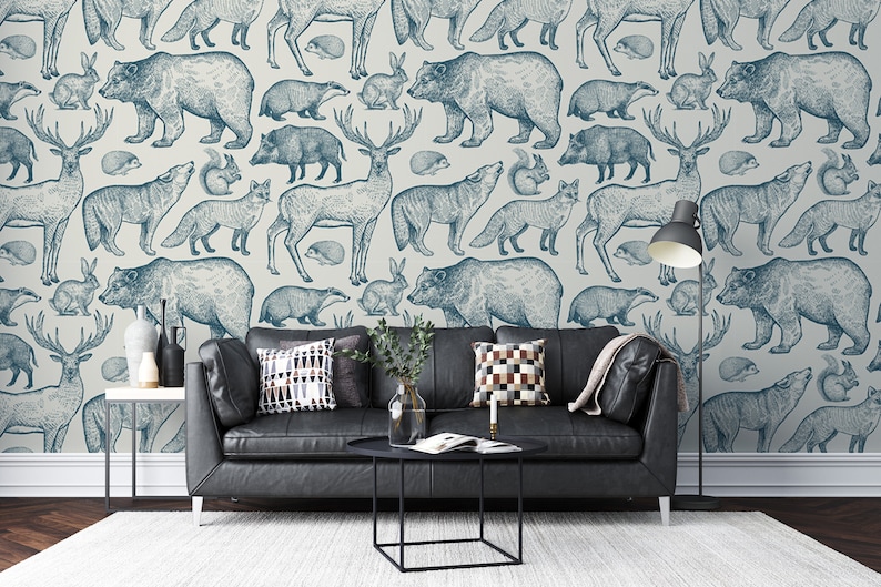 Puede incluir: Un papel tapiz azul y blanco con un patr&oacute;n repetitivo de varios animales del bosque, incluyendo ciervos, osos, lobos, zorros y tejones. El papel tapiz se muestra en un ambiente de sala de estar con un sof&aacute; de cuero negro y una mesa de caf&eacute;.