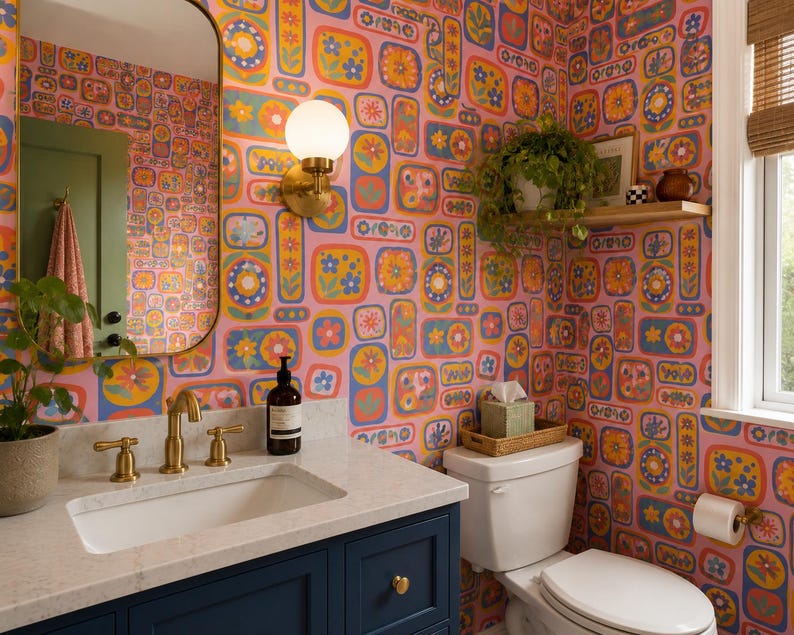 May include: A bathroom with a retro floral wallpaper in pink, yellow, blue, and orange. The room features a white sink with gold fixtures, a navy blue cabinet, and a white toilet. A mirror and a hanging plant add to the decor.