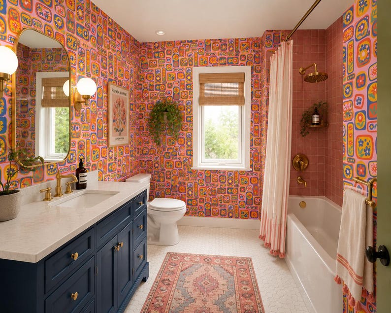 May include: A colorful bathroom with a vibrant floral wallpaper in shades of pink, orange, and blue. Features a navy blue vanity with a white countertop, a white bathtub, and a patterned rug. Gold fixtures and a window with a bamboo shade complete the design.