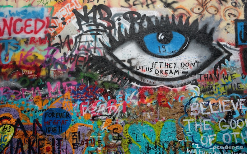 Pode incluir: Uma parede de grafite colorida com um grande olho pintado com uma &iacute;ris azul. O olho &eacute; cercado por v&aacute;rias mensagens e frases, incluindo "If they don't let us dream - than we don't let it the", e "Believe the good of others".