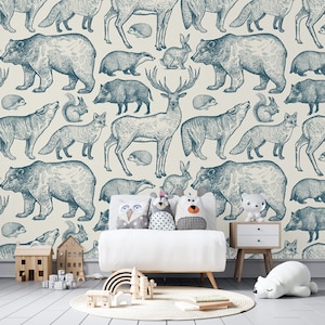 Puede incluir: Una pared blanca con un papel tapiz estampado en azul y blanco que presenta varios animales del bosque, incluidos osos, ciervos, zorros, ardillas y conejos. Un sof&aacute; blanco con tres almohadas se encuentra frente a la pared. Un juguete de arco&iacute;ris de madera y un animal de peluche blanco est&aacute;n en el suelo frente al sof&aacute;.