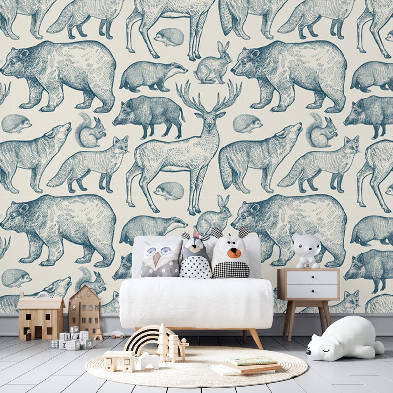 Puede incluir: Una pared blanca con un papel tapiz estampado en azul y blanco que presenta varios animales del bosque, incluidos osos, ciervos, zorros, ardillas y conejos. Un sof&aacute; blanco con tres almohadas se encuentra frente a la pared. Un juguete de arco&iacute;ris de madera y un animal de peluche blanco est&aacute;n en el suelo frente al sof&aacute;.