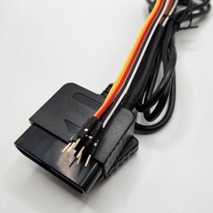 May include: A black connector with a multi-colored wire attached. The wire has red, orange, white, and black wires. The connector has a rectangular shape with a small arrow pointing to the right.