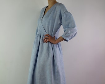 Könnte beinhalten: Ein hellblaues Leinen-Wickelkleid mit V-Ausschnitt und 3/4-Ärmeln. Das Kleid hat einen gerafften Rock und eine lockere Passform.
