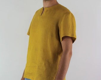Può includere: Camicia di lino giallo senape con scollo a V e maniche corte. La camicia è abbinata a pantaloni azzurri. Il modello è in piedi davanti a uno sfondo bianco. La camicia è realizzata in tessuto leggero.
