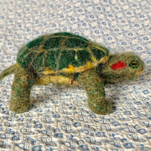 May include: A green, yellow, and brown felt turtle with a red spot on its head.