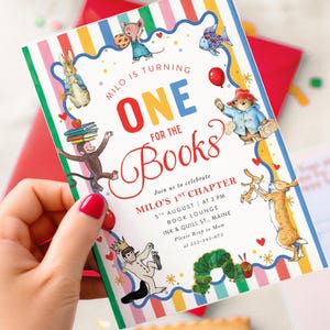 May include: A rectangular birthday invitation card with a colorful vertical striped border featuring illustrations of storybook characters. The text reads: Milo is turning one for the books, join us to celebrate Milo's 1st chapter, 5th August at 2 pm, Book Lounge, Ink & Quill St., Maine, please RSVP to Mom at 555-945-675.
