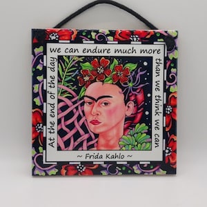 May include: A colorful tile featuring a portrait of Frida Kahlo with flowers in her hair. The tile has a black background with a white border and the quote "we can endure much more than we think we can. At the end of the day ~ Frida Kahlo ~"