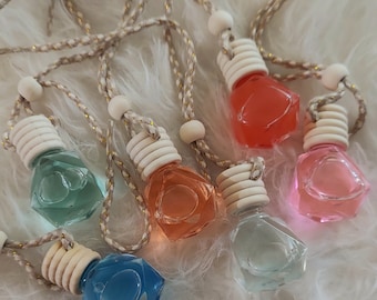 May include: A collection of colorful, small, glass car air fresheners. Each bottle is filled with a different colored liquid and has a wooden cap and a braided rope for hanging. Colors include blue, green, orange, red, and pink.