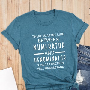 May include: Deep teal t-shirt with the text "THERE IS A FINE LINE BETWEEN NUMERATOR AND DENOMINATOR. ONLY A FRACTION WILL UNDERSTAND." The shirt is paired with blue jeans. The shirt is from Pegasus ApparelUS.