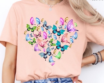 May include: A heather peach t-shirt with a heart-shaped design made up of colorful butterflies. The text "PEGASUS ApparelUS" is printed on the top right corner of the shirt.