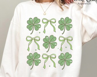 May include: White sweatshirt with a green four-leaf clover and bow design. The design is repeated nine times on the sweatshirt.