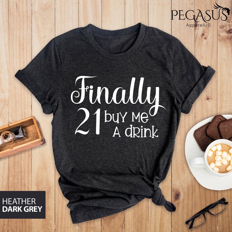 May include: Dark heather grey t-shirt with the text "Finally 21 buy me a drink" in white.