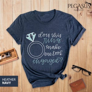May include: A navy blue t-shirt with the text "Does this ring make me look engaged?" in white with a blue diamond ring graphic.