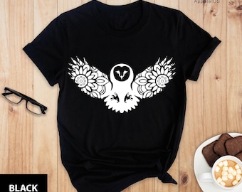 May include: Black t-shirt with a white graphic of an owl with its wings spread out. The owl is surrounded by a mandala design.