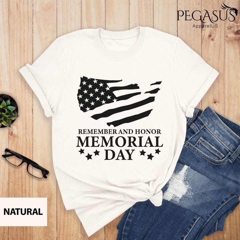 Peut inclure: T-shirt blanc avec un graphique de drapeau am&eacute;ricain noir et blanc et le texte "Remember and Honor Memorial Day" avec trois &eacute;toiles de chaque c&ocirc;t&eacute; du mot "Day".