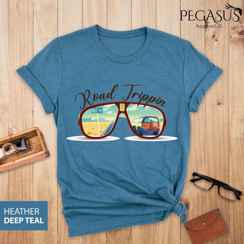 Peut inclure: Un t-shirt bleu avec le texte "Road Trippin" et une paire de lunettes de soleil avec une sc&egrave;ne de route refl&eacute;t&eacute;e dans les verres.
