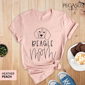 May include: A pink t-shirt with a black outline of a beagle dog and the text "BEAGLE MOM" in black.
