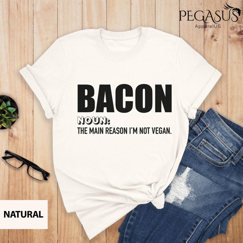 May include: White t-shirt with black text that reads "BACON NOUN: THE MAIN REASON I'M NOT VEGAN."
