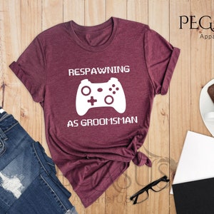 May include: Heather maroon t-shirt with a white graphic of a video game controller and the text "Respawning as groomsman".