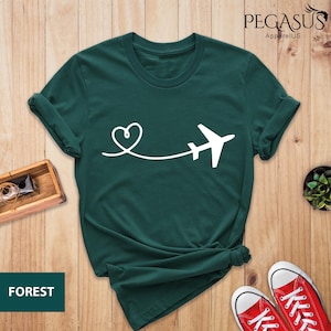 Puede incluir: Una camiseta verde oscuro con un avi&oacute;n y un coraz&oacute;n blancos. El texto "PEGASUS ApparelUS" est&aacute; en la esquina superior derecha de la imagen. El texto "FOREST" est&aacute; en la esquina inferior izquierda de la imagen.