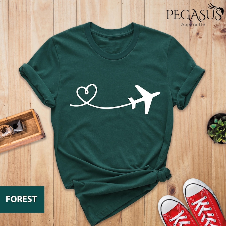 Puede incluir: Una camiseta verde oscuro con un avi&oacute;n y un coraz&oacute;n blancos. El texto "PEGASUS ApparelUS" est&aacute; en la esquina superior derecha de la imagen. El texto "FOREST" est&aacute; en la esquina inferior izquierda de la imagen.