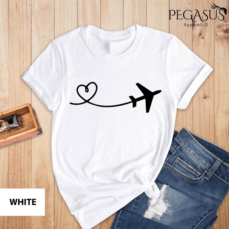 Puede incluir: Camiseta blanca con un gr&aacute;fico de avi&oacute;n y coraz&oacute;n negro. El gr&aacute;fico muestra un coraz&oacute;n con una l&iacute;nea que se extiende a un avi&oacute;n. El texto "PEGASUS ApparelUS" est&aacute; en la esquina superior derecha de la imagen.
