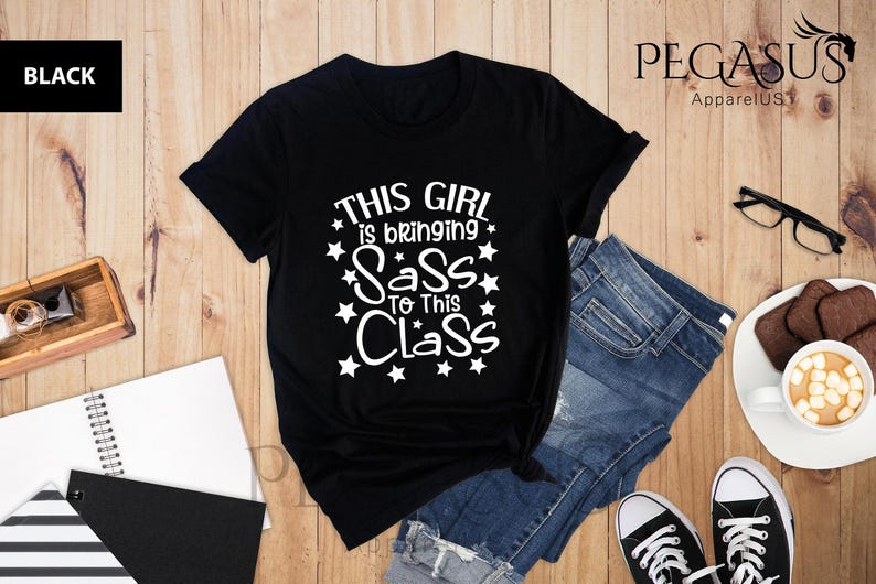 K&ouml;nnte beinhalten: Schwarzes T-Shirt mit wei&szlig;em Text, der "This girl is bringing sass to this class" lautet, mit wei&szlig;en Sternen um den Text herum.