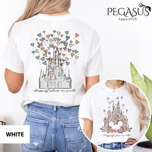 Op de afbeelding: Wit T-shirt met een afbeelding van Assepoester's kasteel met kleurrijke ballonnen en de tekst "Happiest place on earth".
