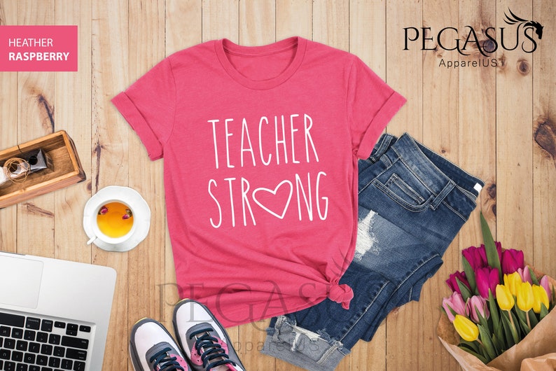 May include: A pink t-shirt with the text "TEACHER STRONG" in white with a white heart in the middle of the word "STRONG".