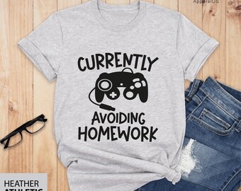 Puede incluir: Una camiseta gris jaspeada con un gráfico negro de un mando de videojuego y el texto "Currently Avoiding Homework".