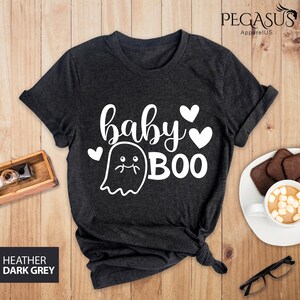 May include: Dark heather grey t-shirt with the words "baby BOO" in white script and a ghost graphic. The shirt also features two white hearts. The text "HEATHER DARK GREY" is in a box in the lower left corner.