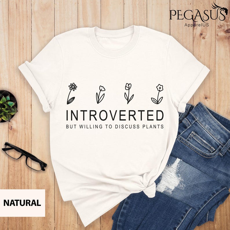May include: White t-shirt with black text that reads "Introverted but willing to discuss plants". The text is surrounded by four simple flower illustrations.