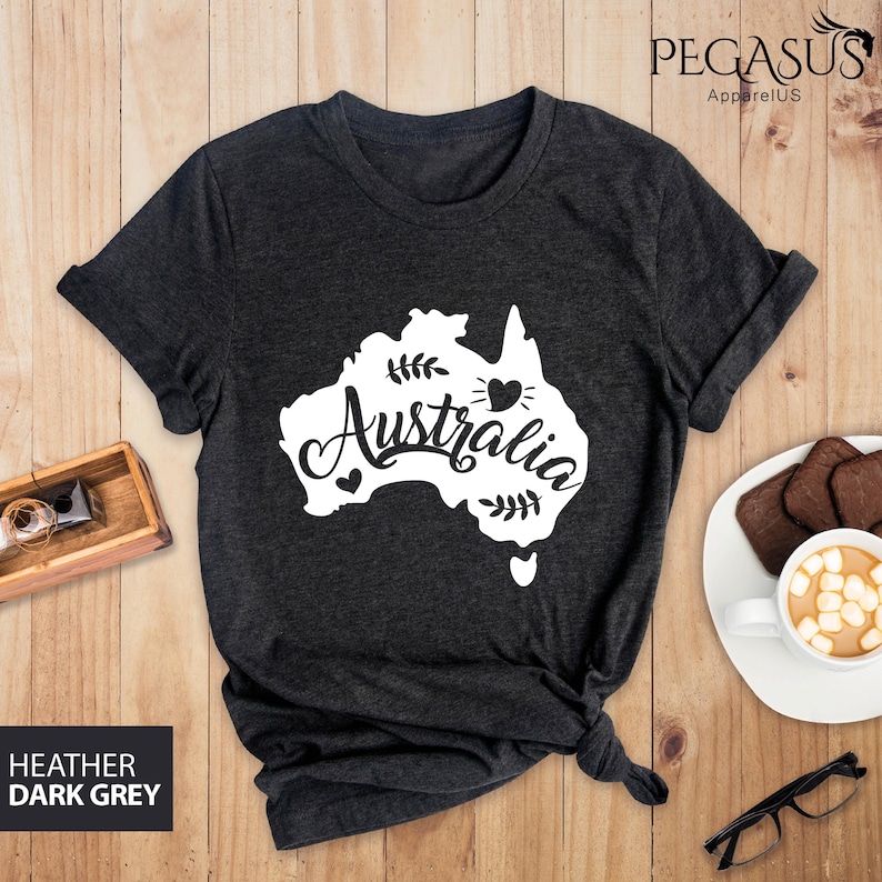 Op de afbeelding: Een donkergrijs t-shirt met een witte omtrek van het continent Australi&euml; en het woord "Australia" in een gestileerd lettertype. Een klein hartje bevindt zich binnen de omtrek van het continent.