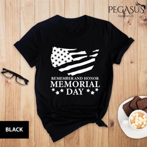 Peut inclure: T-shirt noir avec un graphique blanc d'un drapeau am&eacute;ricain en d&eacute;tresse et le texte "Remember and Honor Memorial Day".