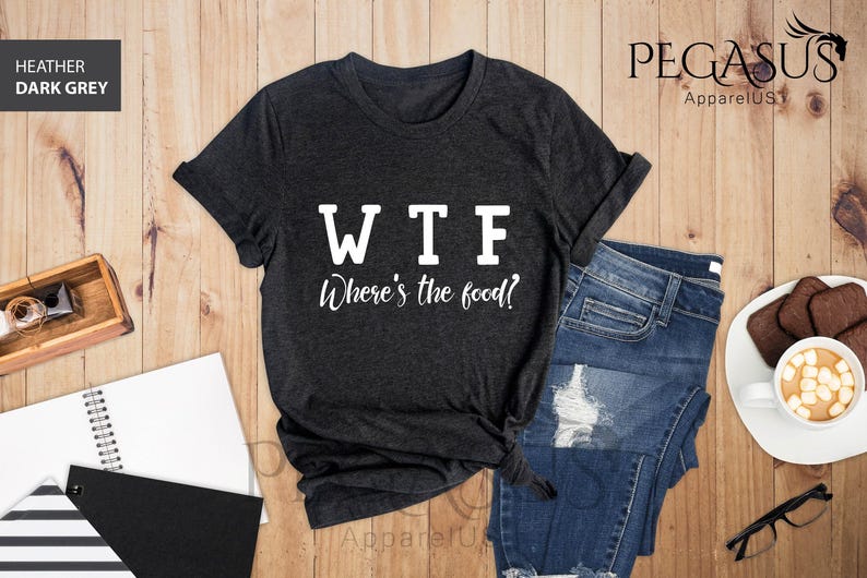 May include: A dark heather grey t-shirt with the text "WTF Where's the food?" printed in white on the front. The shirt is laid flat on a wooden surface with a pair of jeans and a cup of coffee.