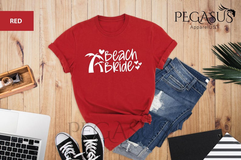 Pu&ograve; includere: Maglietta rossa con testo bianco che dice "Beach Bride" e palme con cuori.