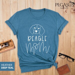 May include: A teal blue t-shirt featuring a white outline of a Beagle dog's head and the text "BEAGLE MOM" in white cursive lettering.