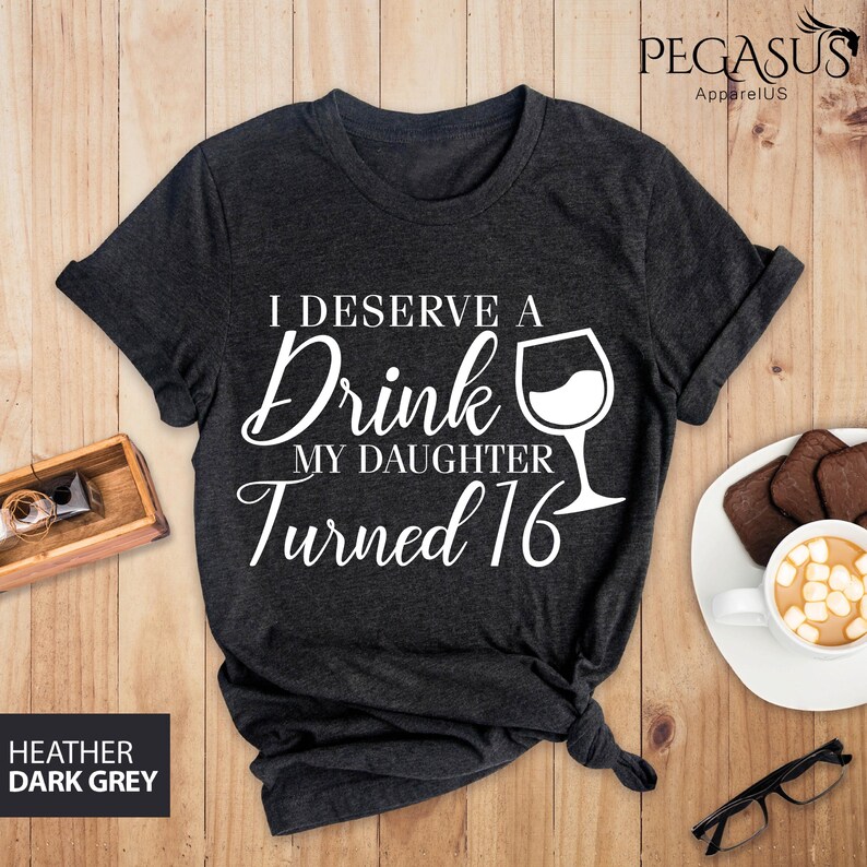 May include: Dark heather grey t-shirt with white text that reads "I deserve a drink my daughter turned 16" and a white wine glass graphic.