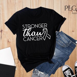 May include: Black t-shirt with white text that reads "Stronger than cancer" and a white ribbon graphic.