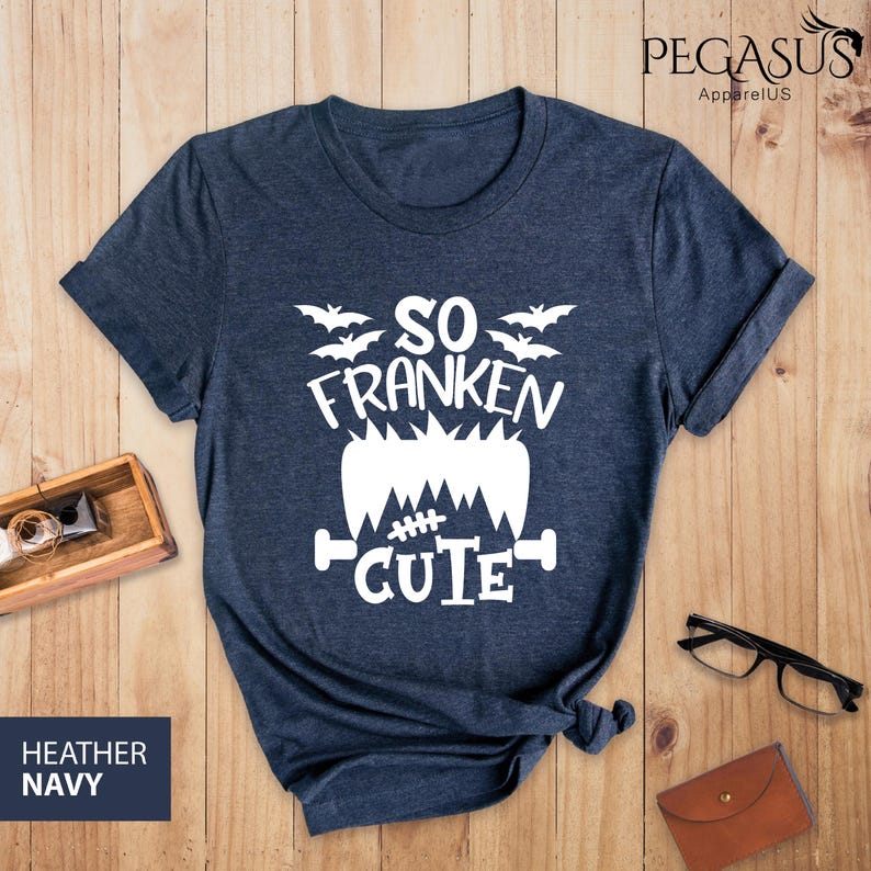 Pu&ograve; includere: T-shirt blu navy melange con grafica bianca che dice "So Franken Cute" con pipistrelli e un design di mostro di Frankenstein. La maglietta ha un girocollo e maniche arrotolate. Il testo "Heather Navy" &egrave; in un riquadro blu navy.