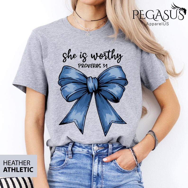 May include: Heather grey t-shirt with a blue bow and the text "She is worthy Proverbs 31" printed on the front.