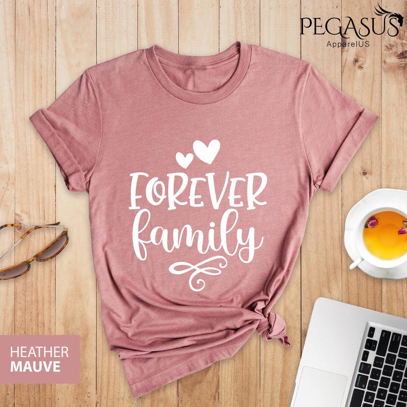 Pode incluir: Uma camiseta de cor malva com o texto "FOREVER family" em letras brancas com dois pequenos cora&ccedil;&otilde;es acima do texto. A camiseta &eacute; feita de um material macio e confort&aacute;vel e &eacute; perfeita para o uso di&aacute;rio.