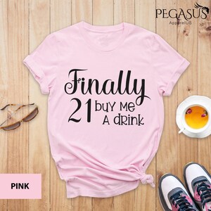 May include: Pink t-shirt with the text "Finally 21 buy me a drink" in black.