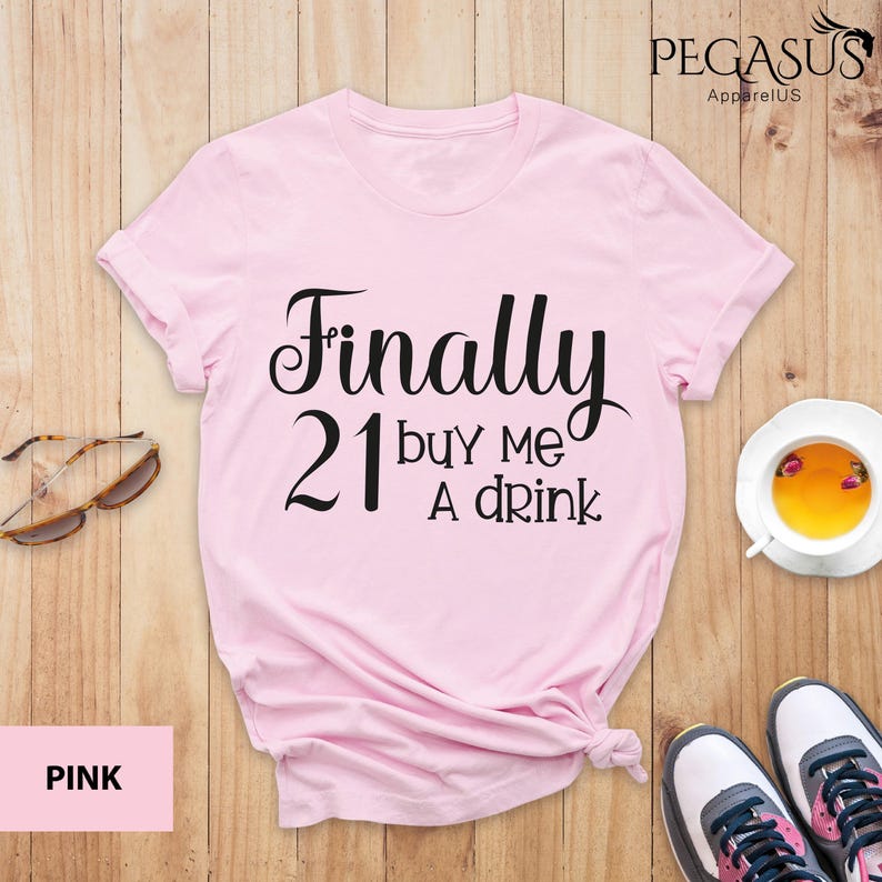 May include: Pink t-shirt with the text "Finally 21 buy me a drink" in black.